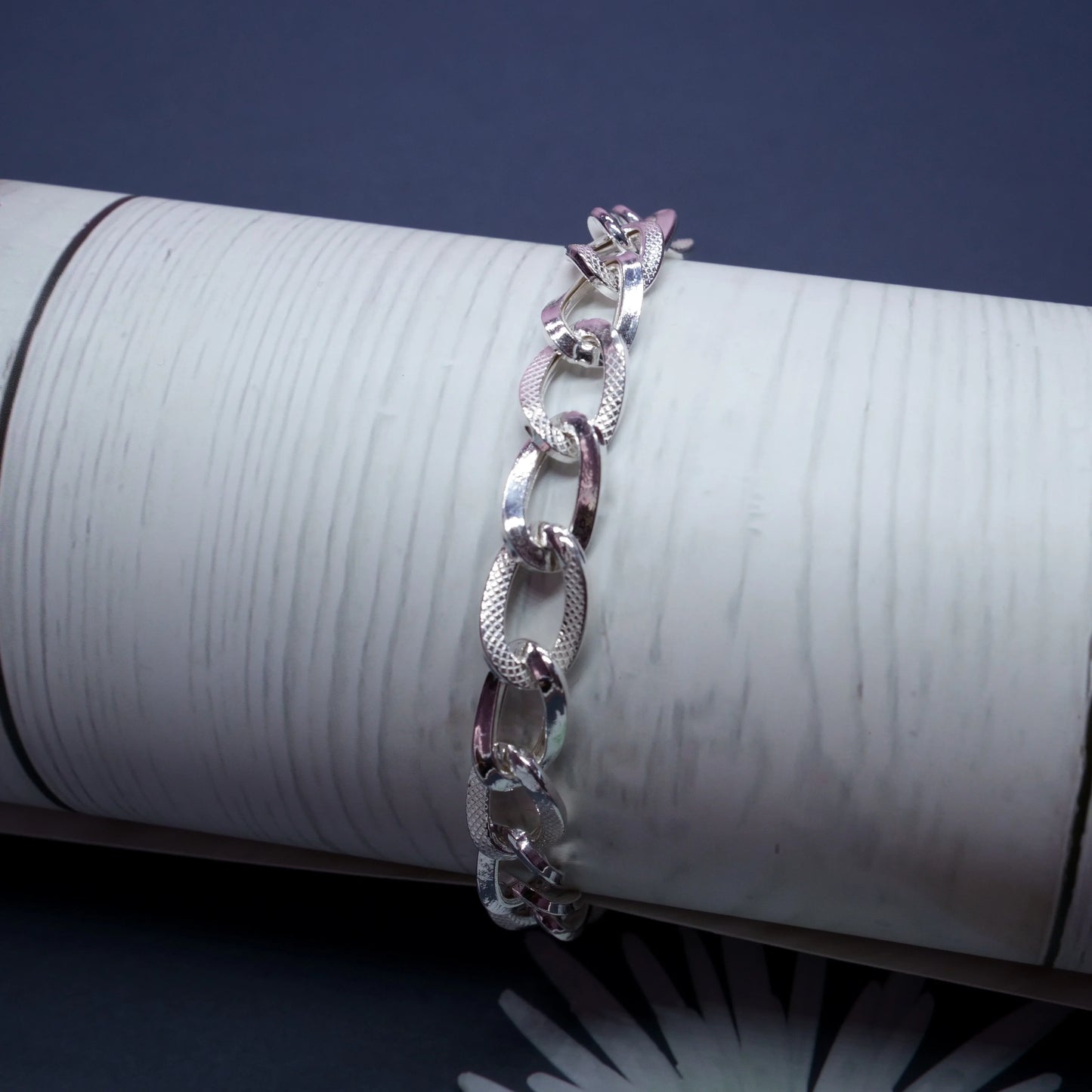 Silver textured chain link bracelet displayed on white cylindrical stand against dark background