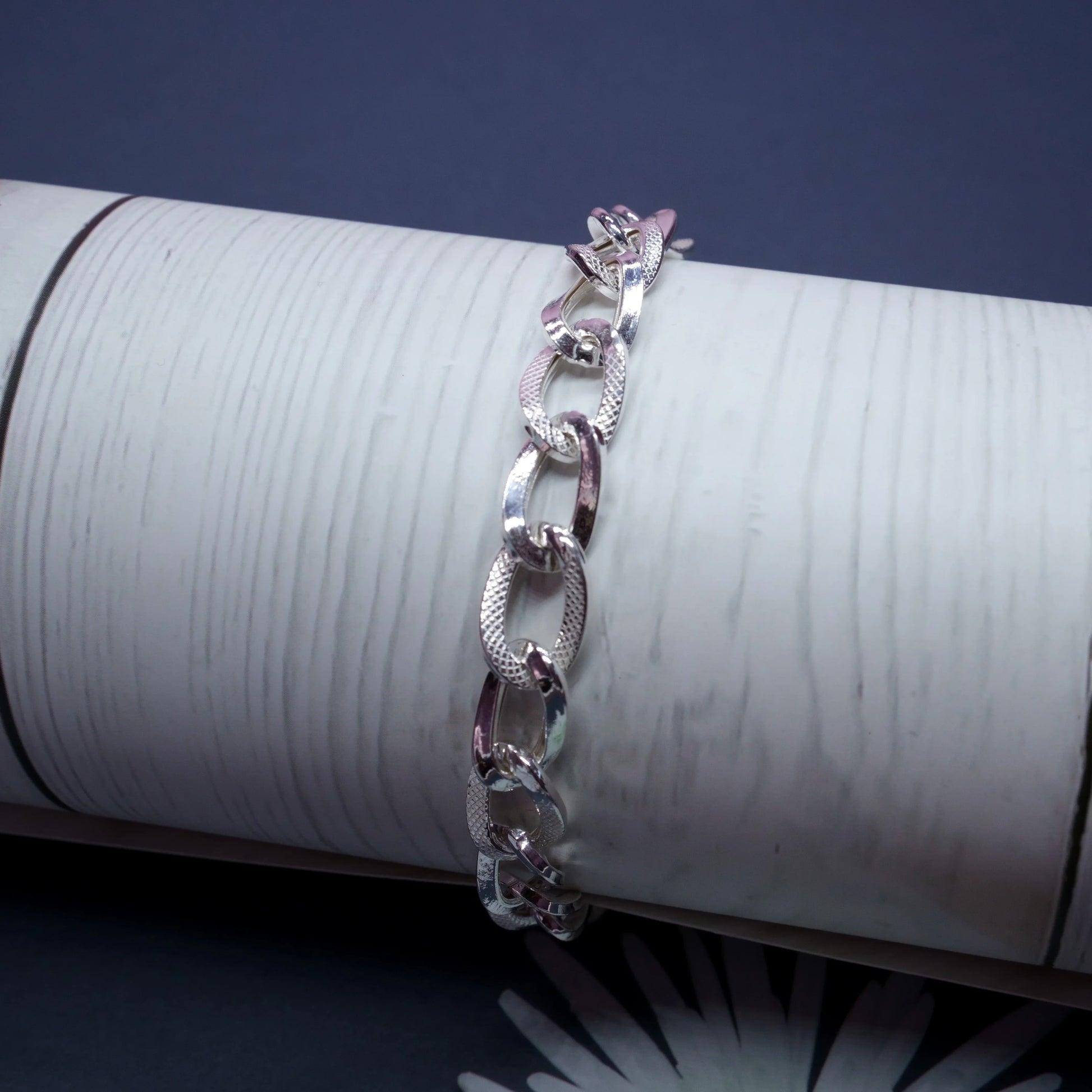 Silver textured chain link bracelet displayed on white cylindrical stand against dark background