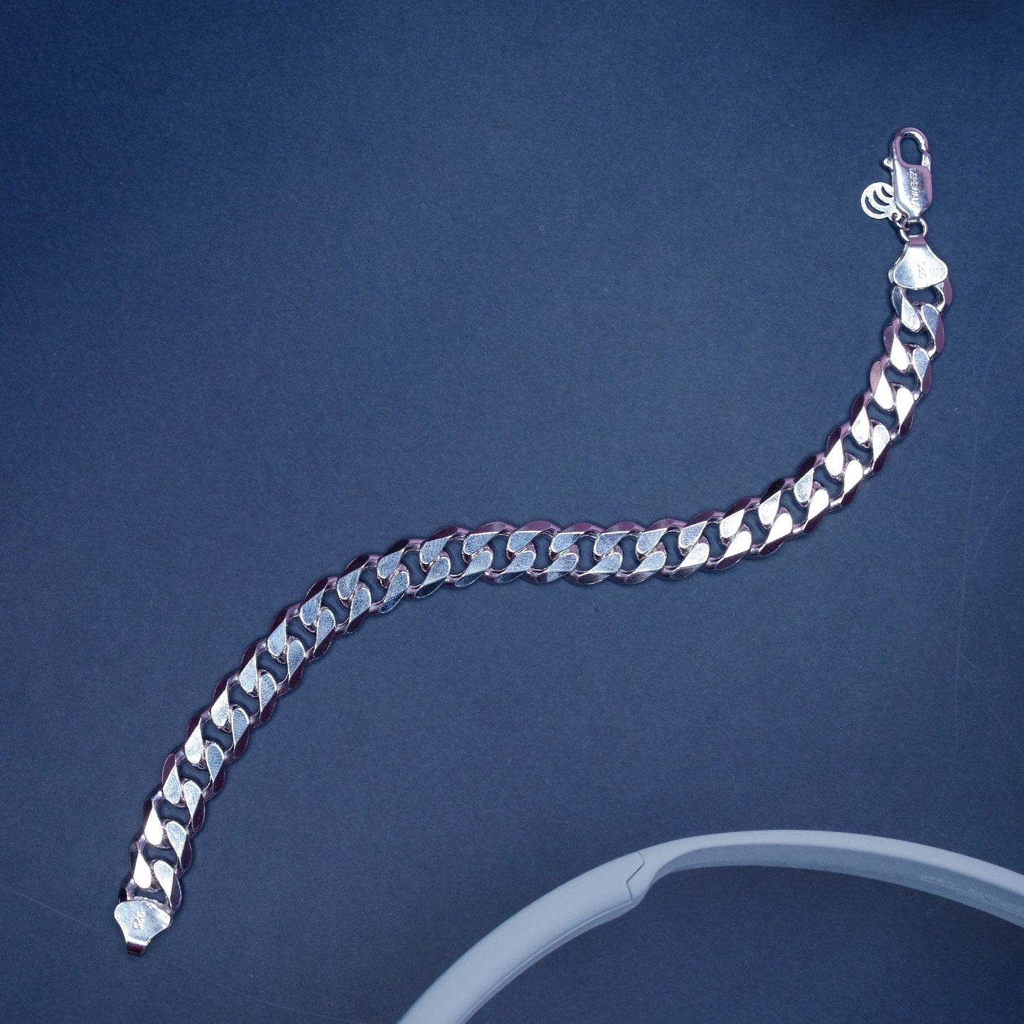 silver Cuban link bracelet with clasp on dark background and partial white circular object