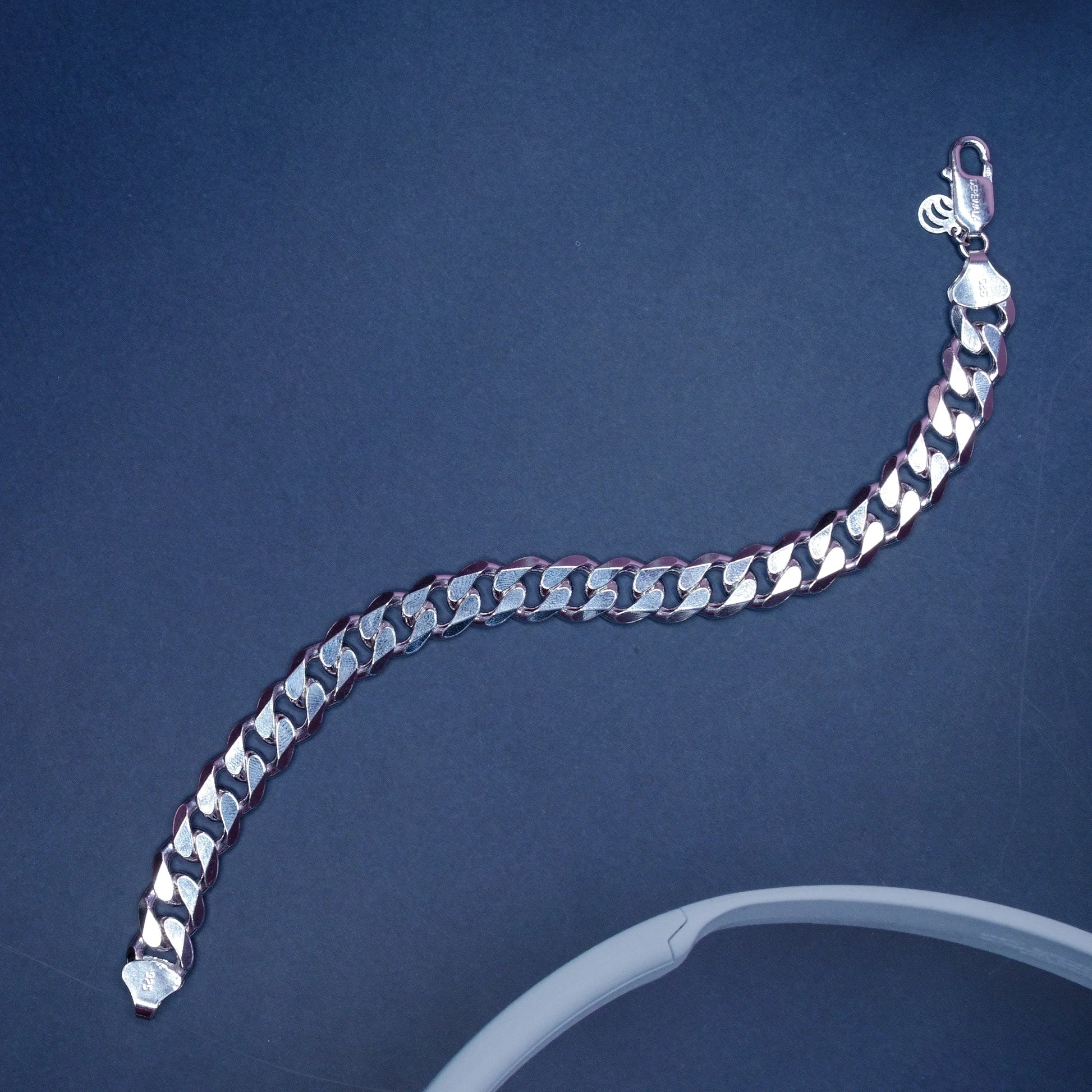 silver Cuban link bracelet with clasp on dark background and partial white circular object
