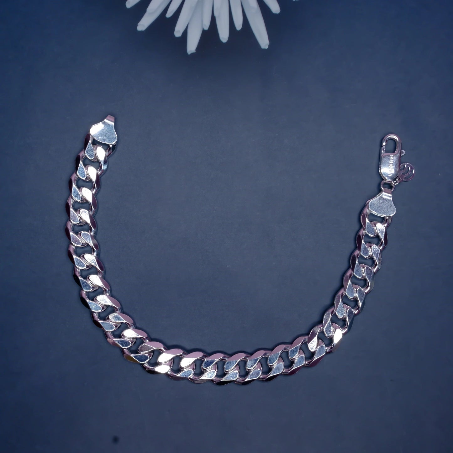 Silver Cuban link chain bracelet on dark background with white flower decoration