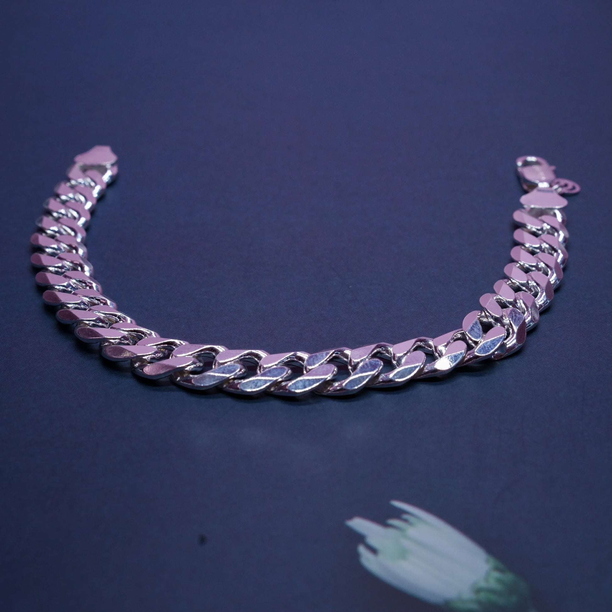 silver Cuban link chain bracelet on dark blue surface with white flower detail