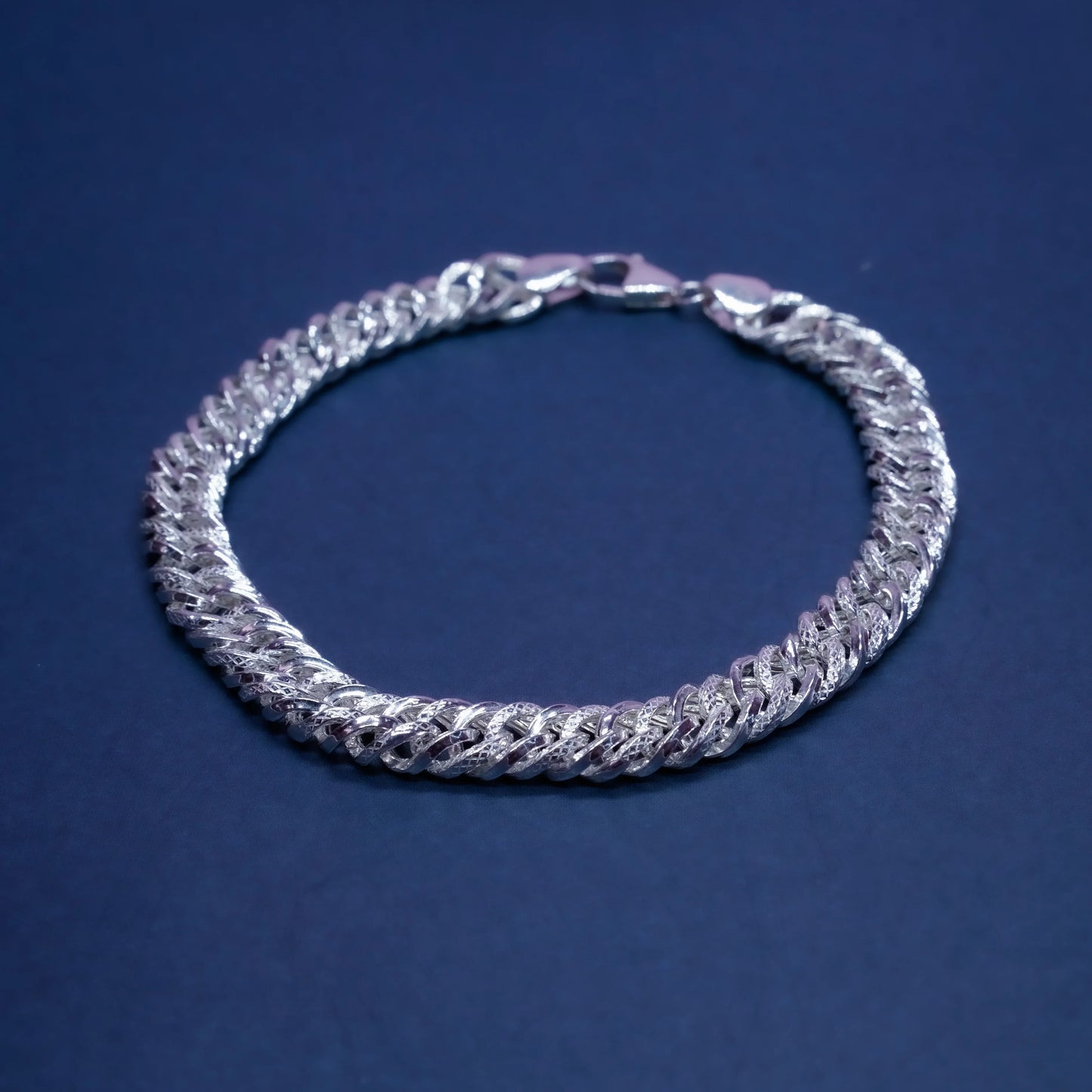 Silver Cuban link chain bracelet on a dark blue background with polished and textured links