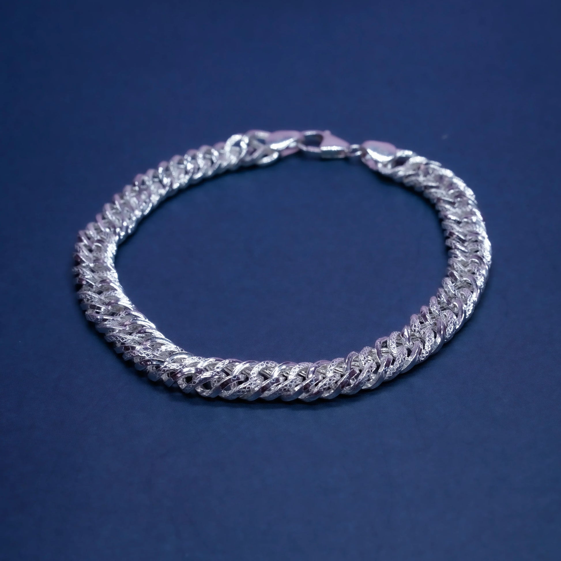 Silver Cuban link chain bracelet on a dark blue background with polished and textured links