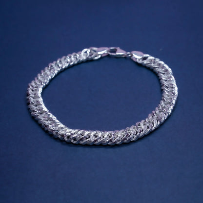 Silver Cuban link chain bracelet on a dark blue background with polished and textured links