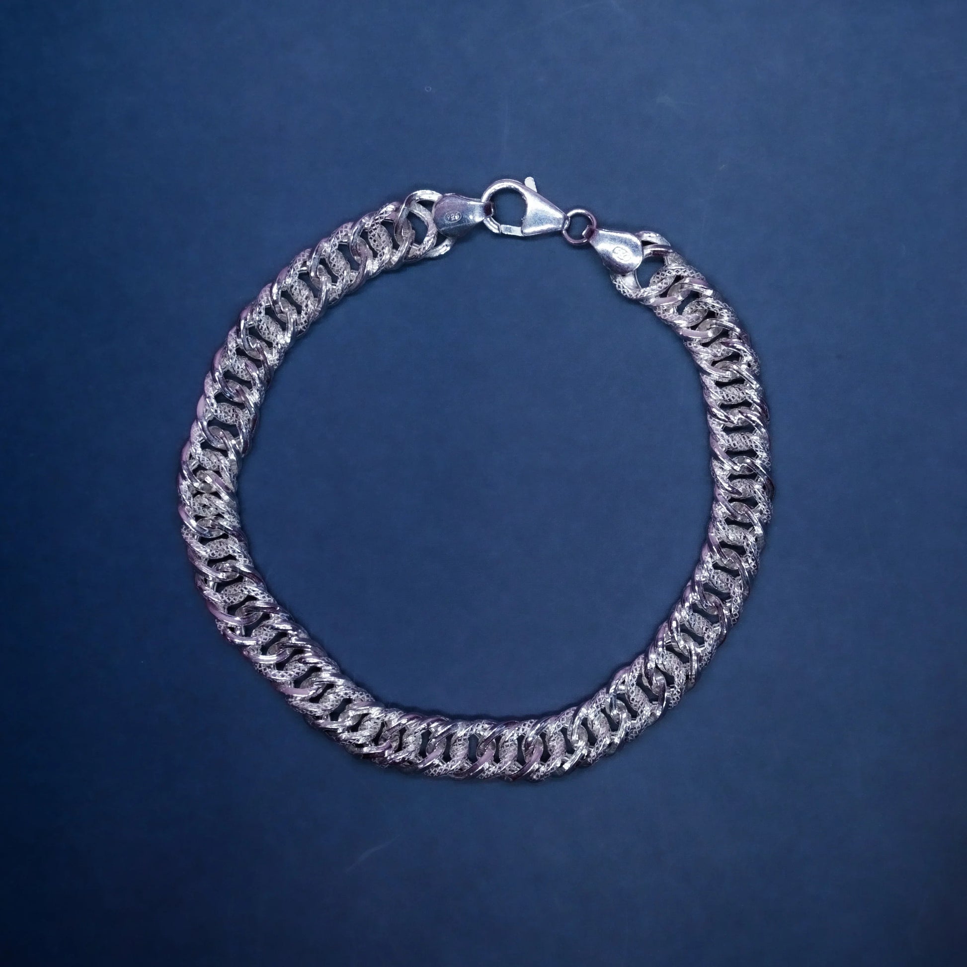 silver Cuban link chain bracelet with lobster clasp on dark blue background