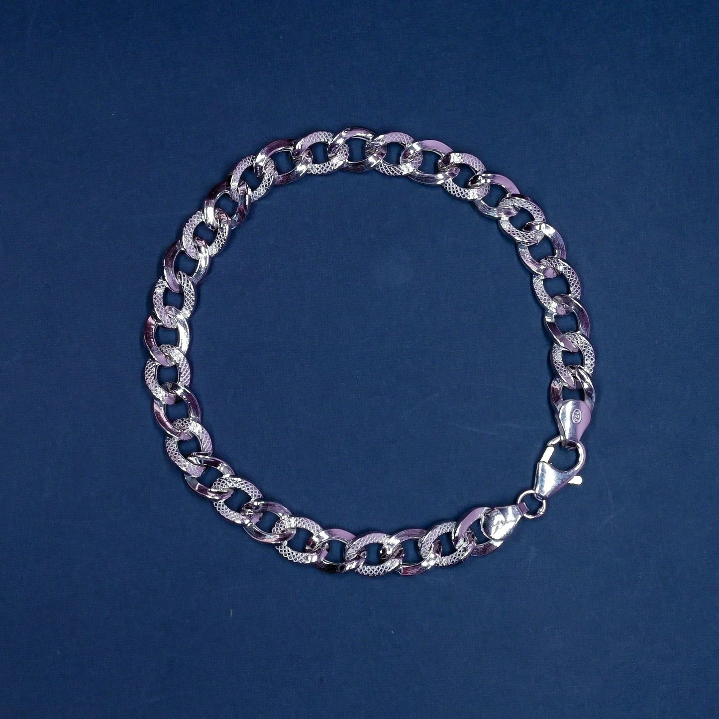 Silver chain bracelet with textured and smooth oval links on a dark blue background