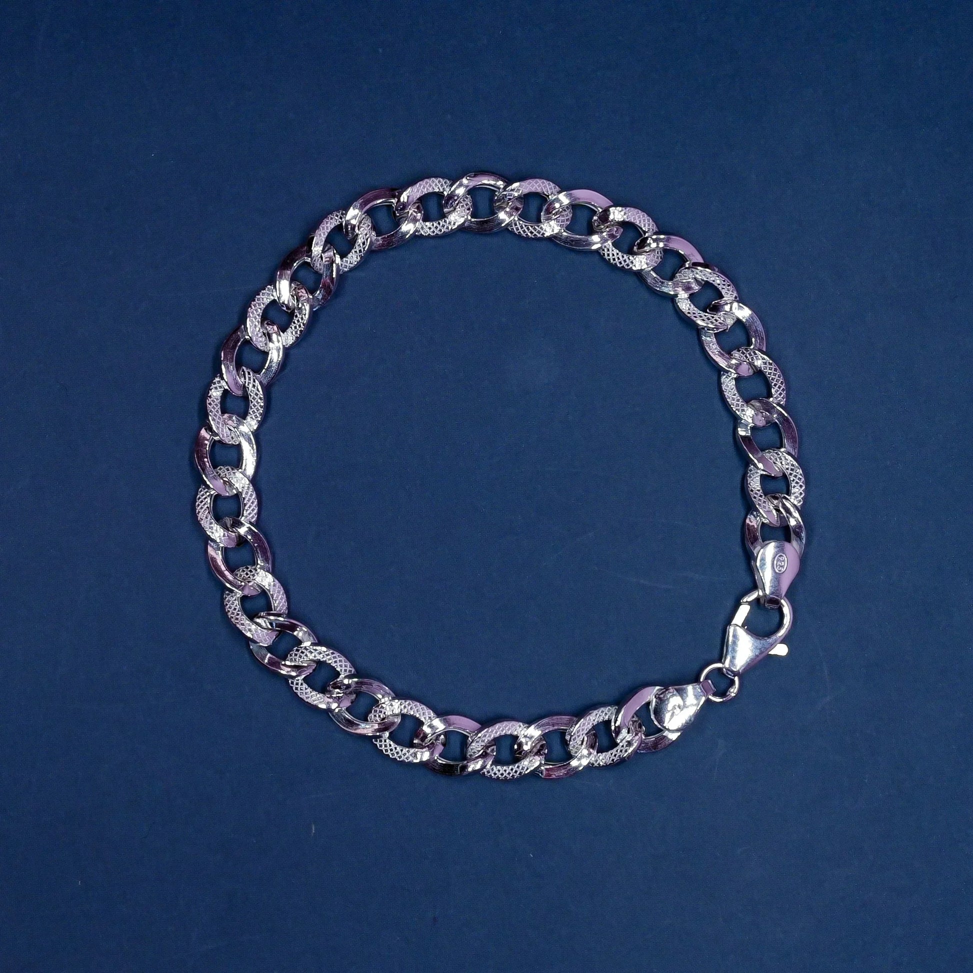 Silver chain bracelet with textured and smooth oval links on a dark blue background