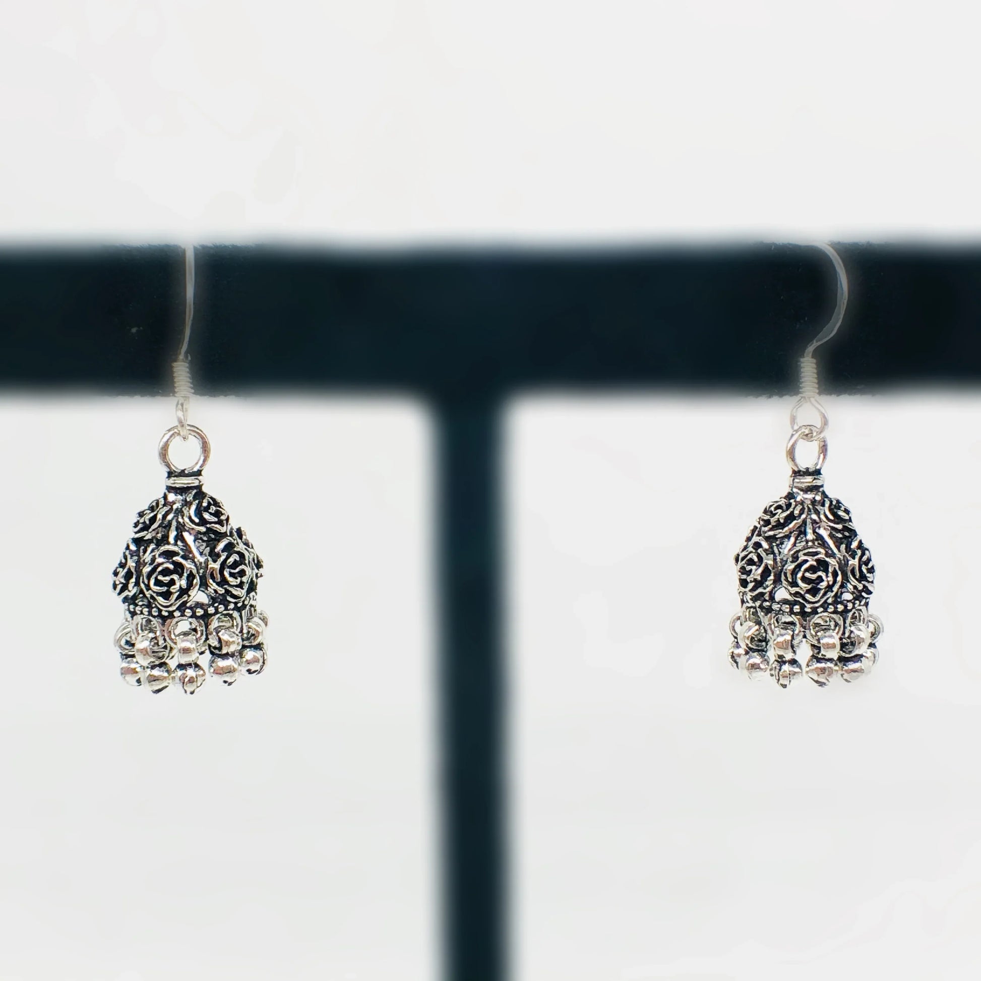 Pair of oxidized silver jhumka earrings with intricate floral design and dangling beads