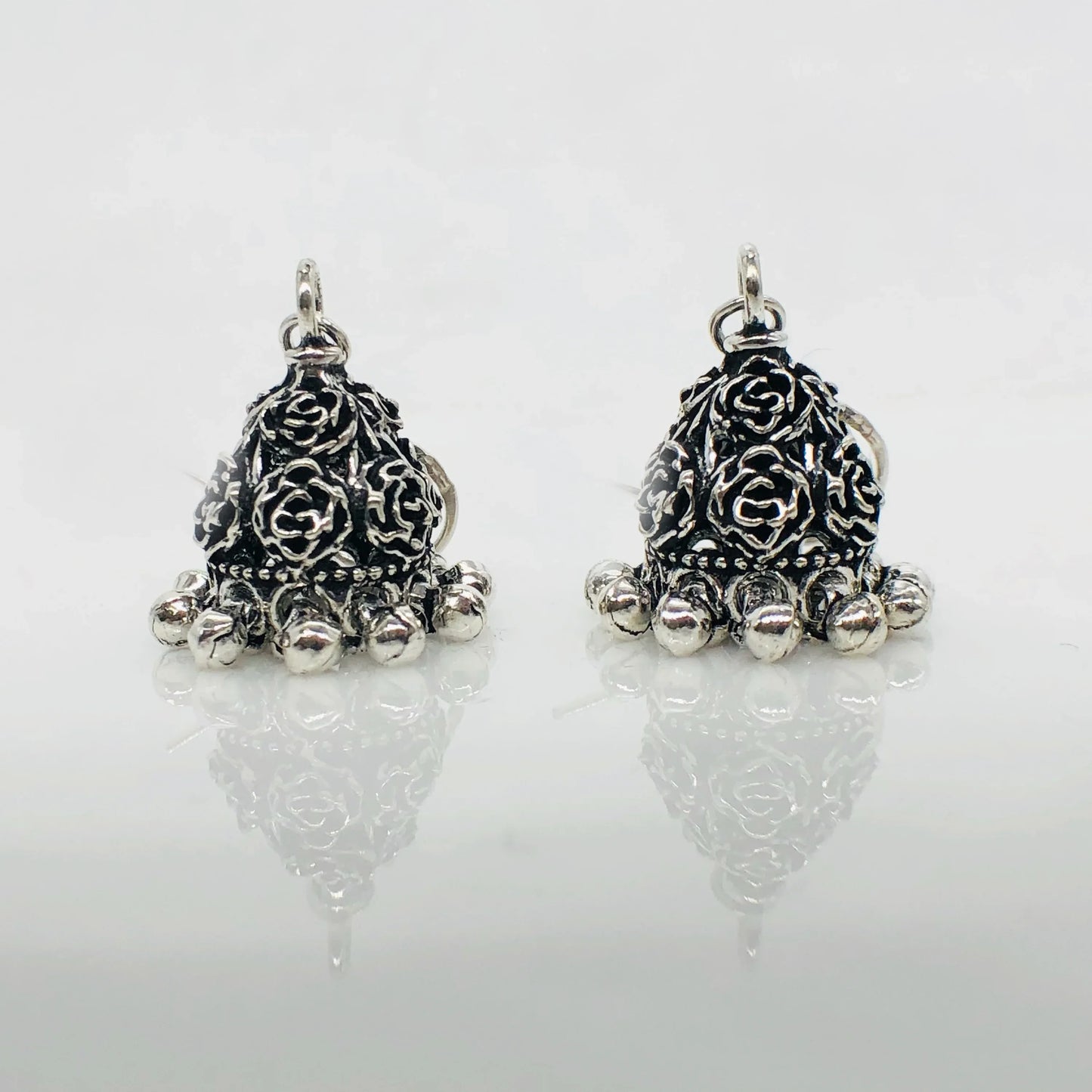 Pair of silver oxidized jhumka earrings with floral engravings and dangling beads on white background
