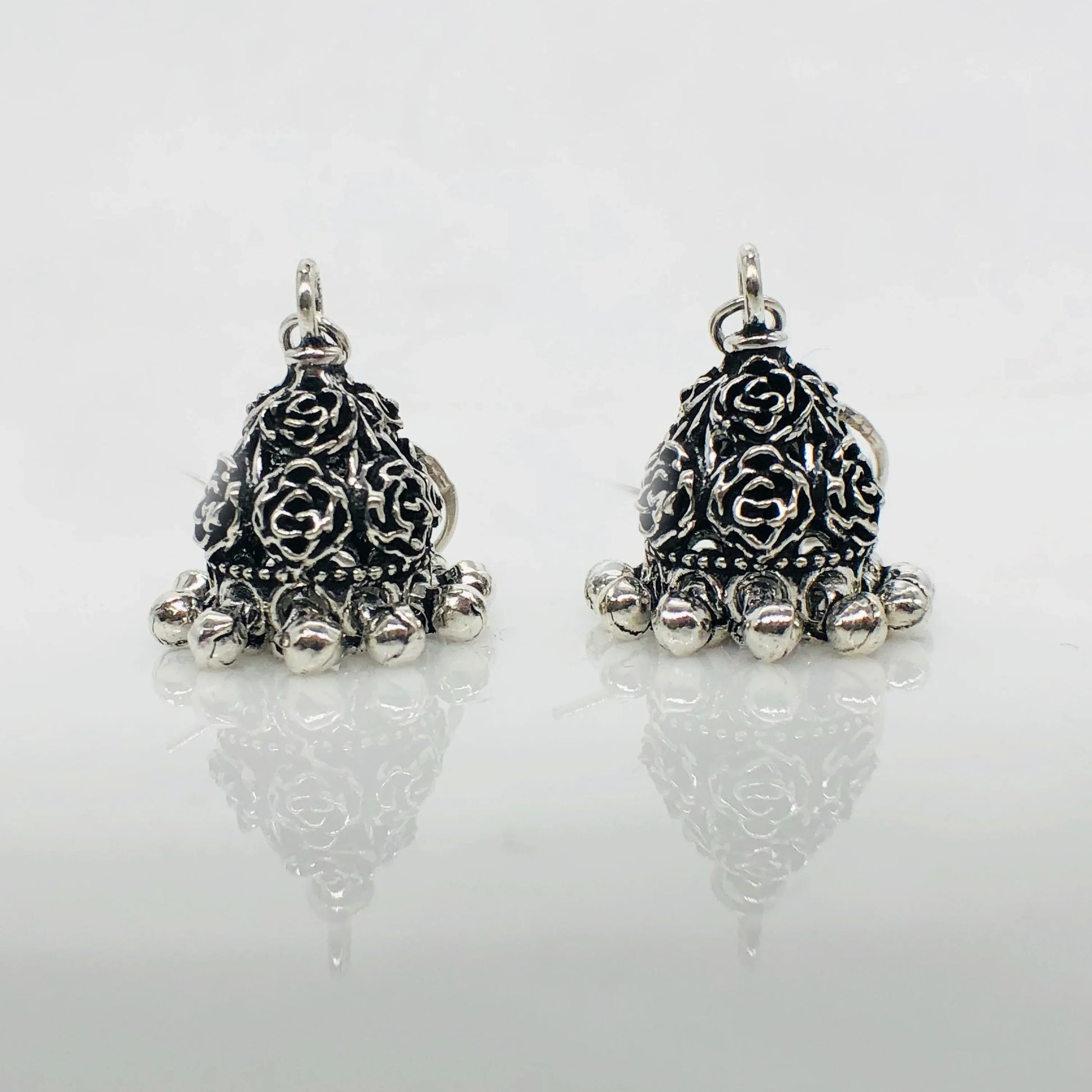 Pair of silver oxidized jhumka earrings with floral engravings and dangling beads on white background