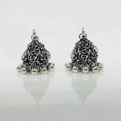 Pair of silver oxidized jhumka earrings with floral engravings and dangling beads on white background