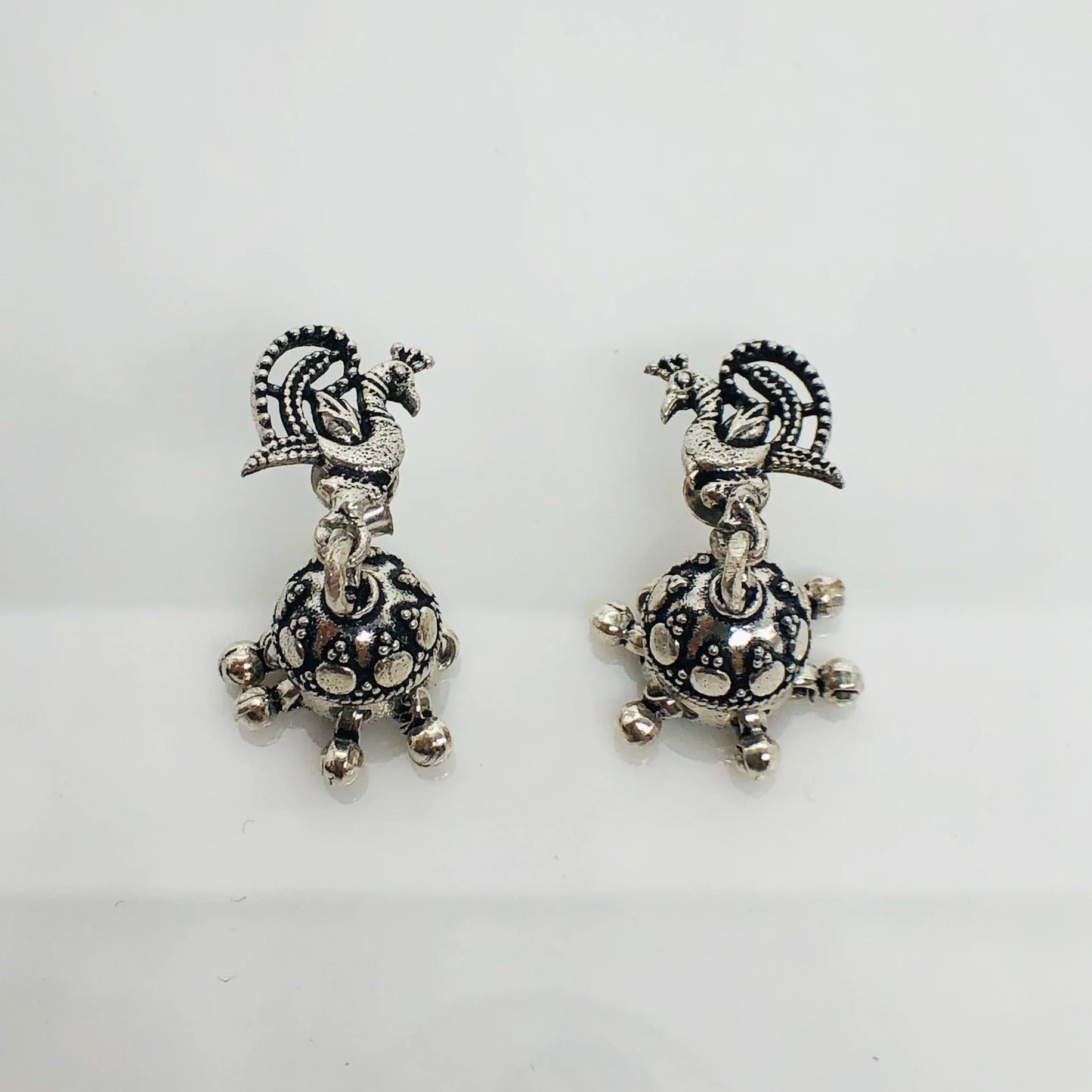 Pair of oxidized silver earrings with intricate peacock design and dangling decorative elements