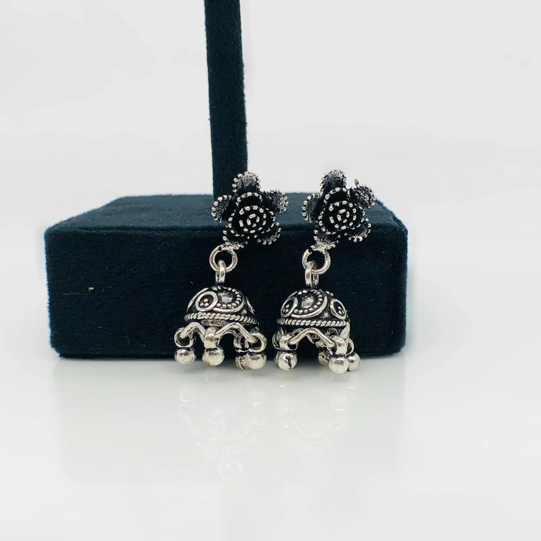 Silver oxidized jhumka earrings with floral stud design on black display stand