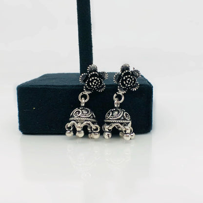 Silver oxidized jhumka earrings with floral stud design on black display stand